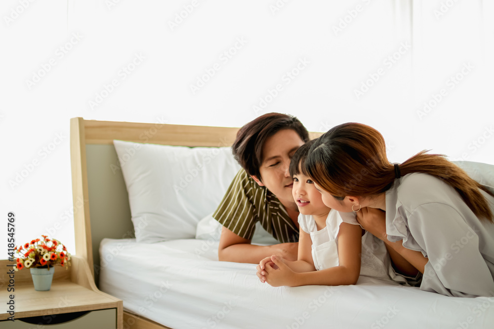 happy family having fun in bed room concept. father,mother and daugther smiling face, kiss love together lying on bed with duvet cover them copy space.