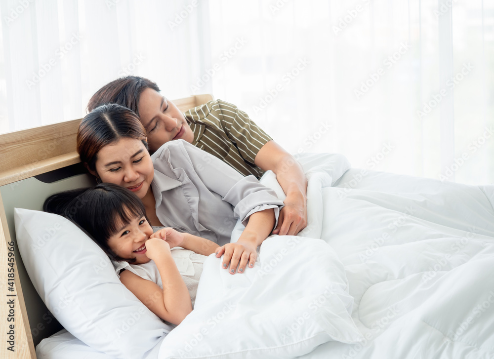 happy family having fun in bed room concept. father,mother and daugther smiling face, kiss love together lying on bed with duvet cover them copy space. happy family having fun in bed room concept. father,mother and daugther smiling face, kiss love together lying on bed with duvet cover them copy space.