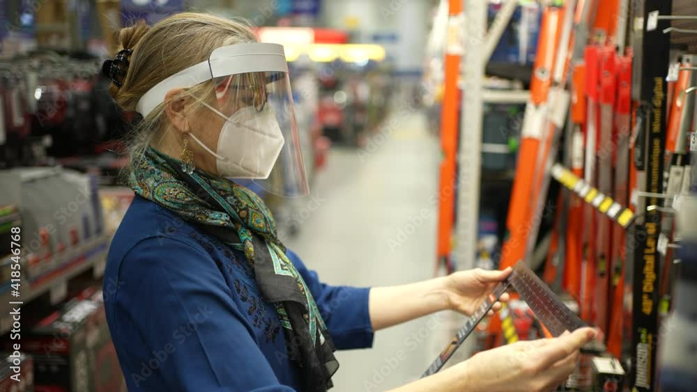 Woman wearing ppe face shield and mask shopping for flooring in a hardware store during pandemic. Concept of shopping wearing personal protection equipment. Woman wearing ppe face shield and mask shopping for flooring in a hardware store during pandemic. Concept of shopping wearing personal protection equipment.
