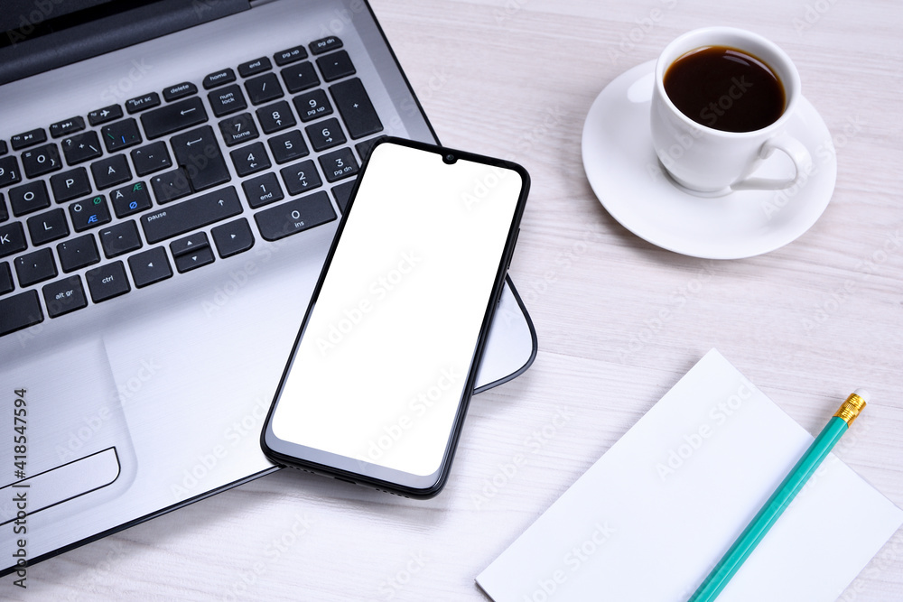 Smartphone, mobile phone with white screen on a gray laptop on the desktop. Mock up Smartphone, mobile phone with white screen on a gray laptop on the desktop. Mock up