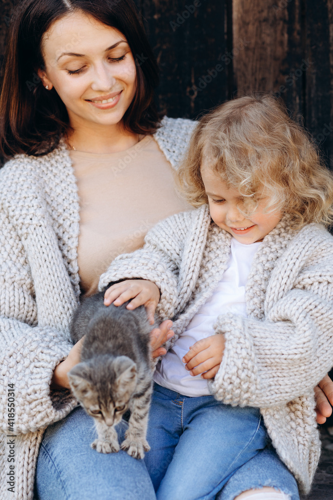 Mother and her daughter play with a little cat by the wooden wall. Mother and her daughter play with a little cat by the wooden wall.