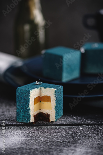 Blue cake filled with orange and tangerine in the shape of a cube. Nearby on a black table are ingredients oranges, tangerines, nuts. Rustic style.
