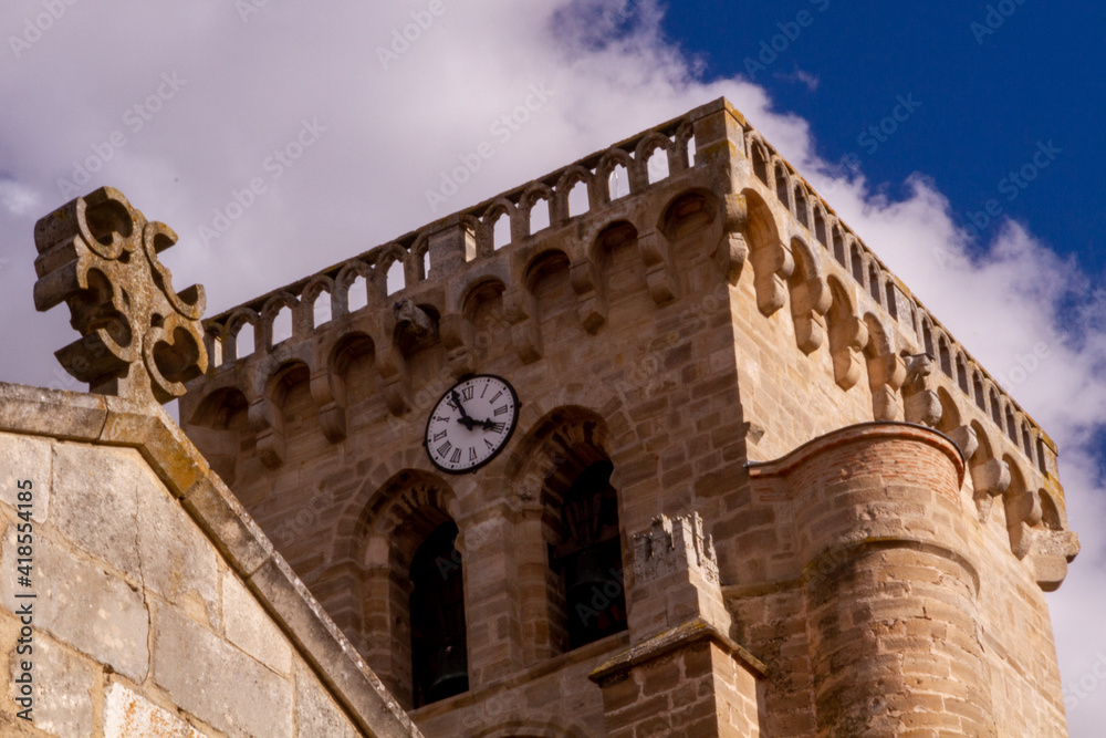 A cross on the top of a roof in front of a clock tower