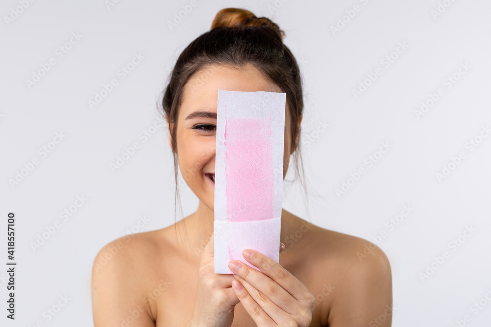 Body care, caucasian happy woman closed her face with waxing strip for hair removal. Pretty woman studio portrait isolated on gray background. Depilation concept. Home routine. Body care, caucasian happy woman closed her face with waxing strip for hair removal. Pretty woman studio portrait isolated on gray background. Depilation concept. Home routine.