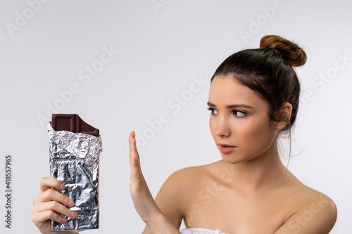 A woman making hand sign to refuse, holding a chocolate bar. I am against eating foods fat. Power woman refuses to consume delicious tasty sweets isolated on bright gray background