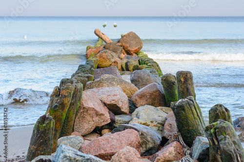 Old breakwater in sea. Wooden piles covered with algae and moss. Large stones inside structure. Beautiful seascape, selective focus