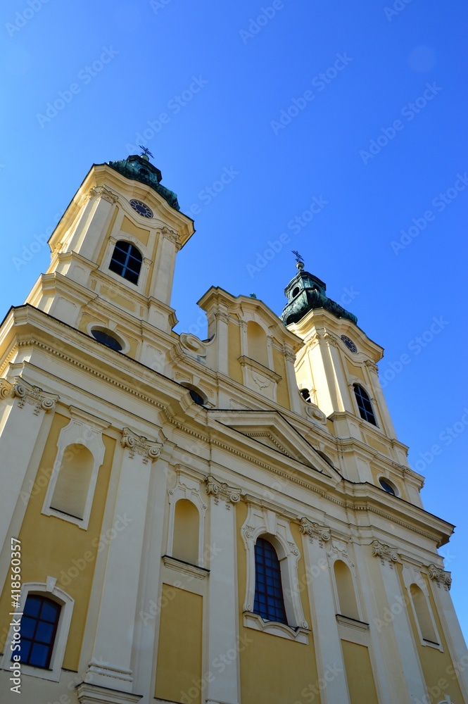 Baroque two-towered piarist church of St. Ladislav in Nitra, viewed from the street, spring clear blue skies. Jet trail and part of parking sign is visible in upper and lower right corner