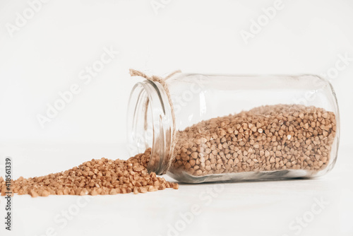 Buckwheat in a glass jar scattered on a wooden white table. Copy, empty space for text