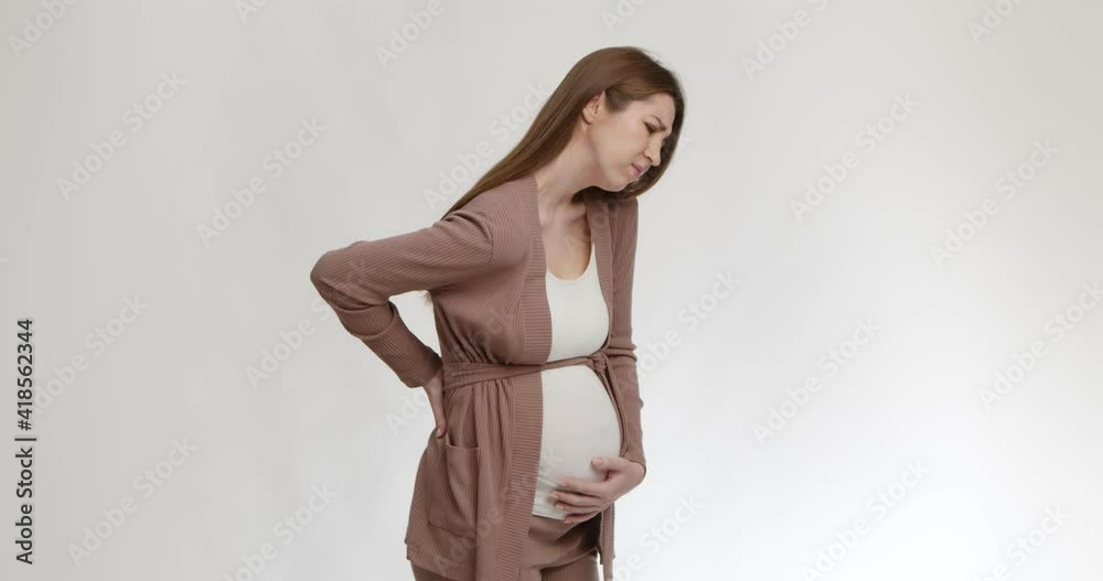 Hardships of pregnancy. Young pregnant lady suffering from backache, holding her belly and touching inflamed loins Hardships of pregnancy. Young pregnant lady suffering from backache, holding her belly and touching inflamed loins