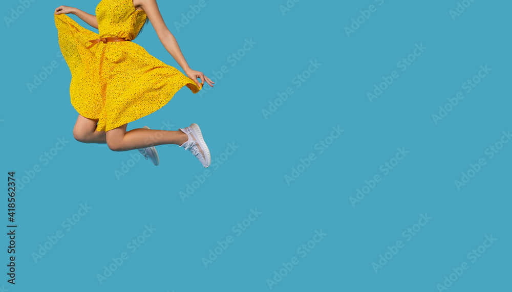Girl with yellow dress jumping in the air isolated on blue background. Life people energy concept Girl with yellow dress jumping in the air isolated on blue background. Life people energy concept