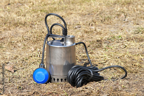 Well pump with a long black cable on the background of old grass. Pump with power cable and external blue float switch.