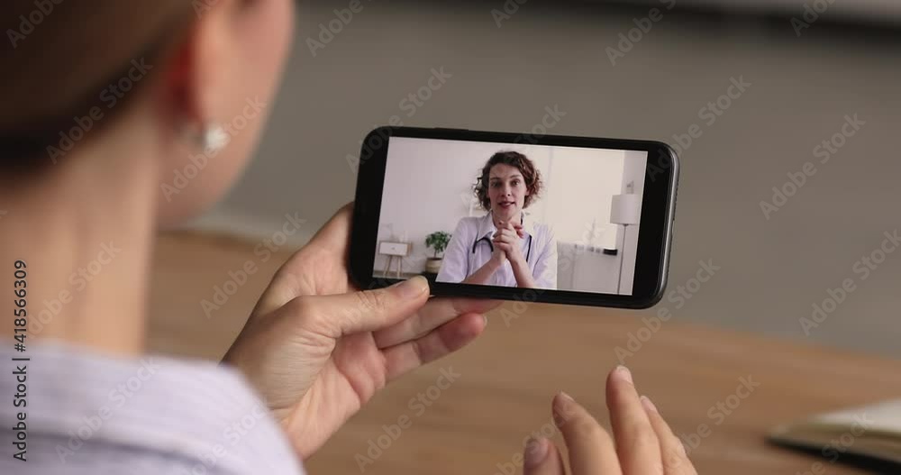 Close up focus on telephone with skilled trusted female general practitioner in white coat giving professional medic consultation or healthcare advices by video call zoom meeting to patient distantly.