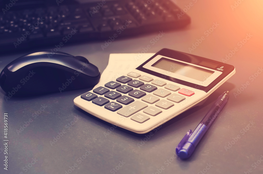 Calculator, pen, computer lie on the desk. Business Financing Accounting Banking Concept. Tinted photograph. Calculator, pen, computer lie on the desk. Business Financing Accounting Banking Concept. Tinted photograph.