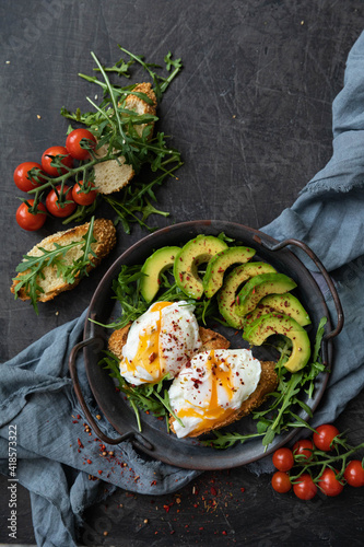 Breakfast with poached egg, avocado and arugula. with fried toast and cherry tomatoes, served in a cast-iron pan on a textile background. Top view