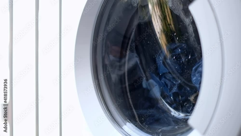 the laundry is washed in a white automatic washing machine behind a glass door, the metal drum rotates in different directions in turn. washing clothes jeans. homework 4k the laundry is washed in a white automatic washing machine behind a glass door, the metal drum rotates in different directions in turn. washing clothes jeans. homework 4k