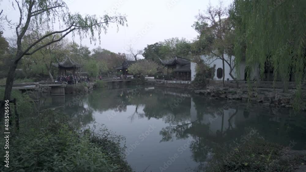 Panning shot of people exploring structures by pond by trees at park against sky - Suzhou, China Panning shot of people exploring structures by pond by trees at park against sky - Suzhou, China