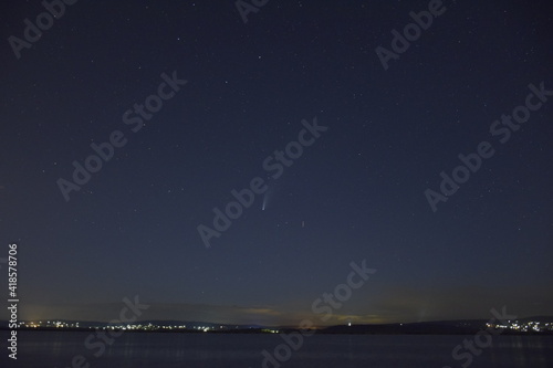 neowise comet flying across the night sky above a lake