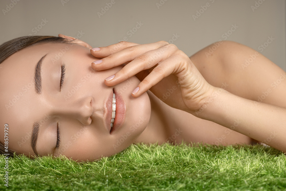 portrait of a beautiful white skin natural looking girl massaging her face with fingers on a green grass portrait of a beautiful white skin natural looking girl massaging her face with fingers on a green grass