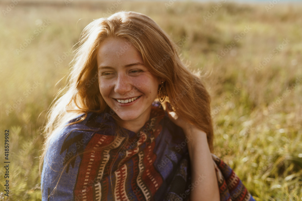 Naklejka premium On the meadow grass sits a beautiful girl without makeup with freckles on her face smiling broadly with a white-toothed smile. High quality photo