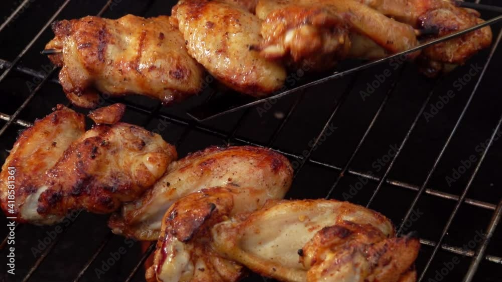 The appetizing chicken wings on the wooden skewers are frying and roasting above the open fire outdoors The appetizing chicken wings on the wooden skewers are frying and roasting above the open fire outdoors