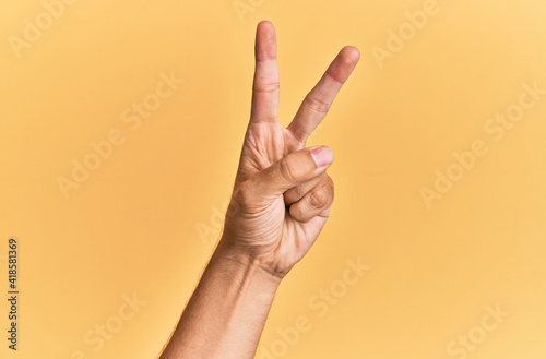 Arm and hand of caucasian man over yellow isolated background counting number 2 showing two fingers, gesturing victory and winner symbol photo