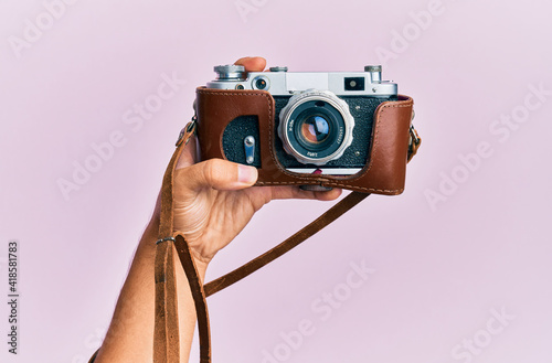 Hand of young hispanic man holding vintage camera over isolated pink background.