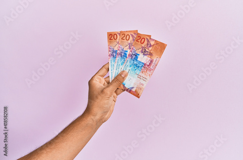 Hispanic hand holding 20 swiss franc banknotes over isolated pink background.