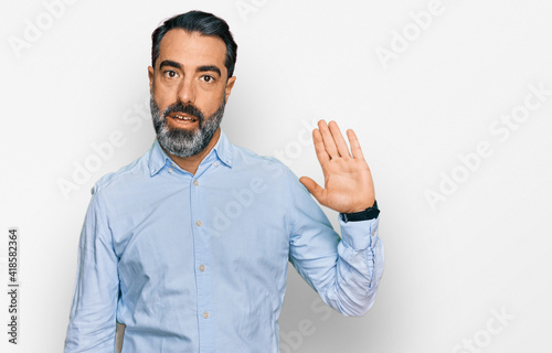 Middle aged man with beard wearing business shirt waiving saying hello happy and smiling, friendly welcome gesture