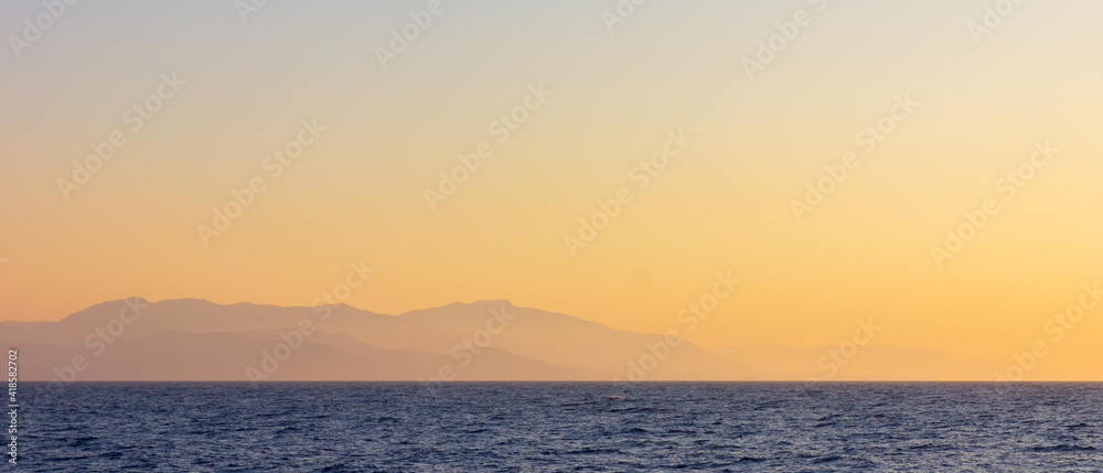 Seascape with fog and mountains. Seascape at sunset. View from the sea to the mountains in the haze. Dramatic scenes and the beauty of nature. Copy space