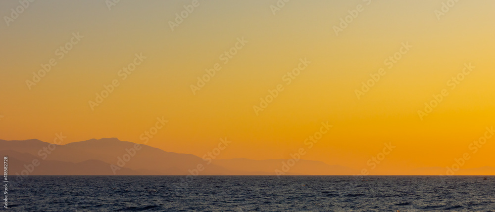 Obraz premium Seascape with fog and mountains. Seascape at sunset. View from the sea to the mountains in the haze. Dramatic scenes and the beauty of nature. Copy space