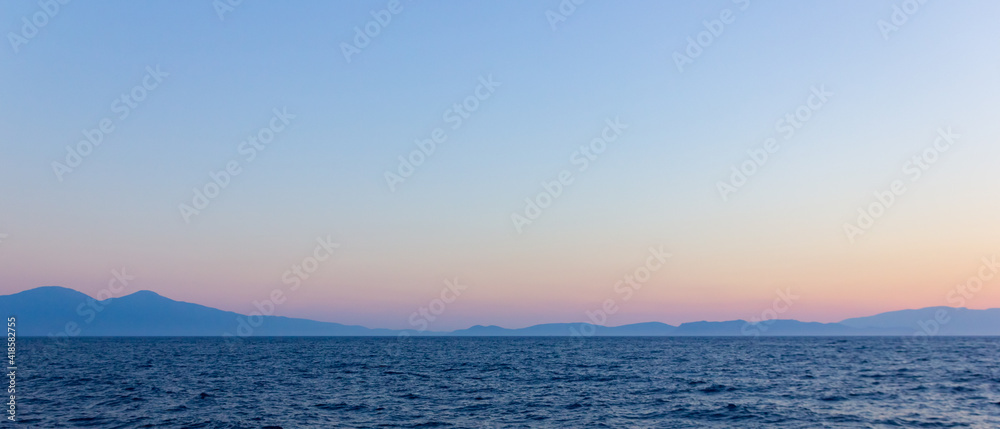 Seascape with fog and mountains. Seascape at sunset. View from the sea to the mountains in the haze. Dramatic scenes and the beauty of nature. Copy space