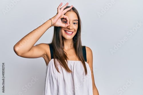 Young hispanic woman wearing casual clothes smiling happy doing ok sign with hand on eye looking through fingers