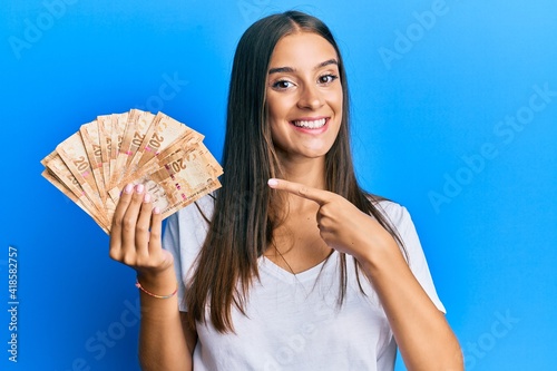 Young hispanic woman holding south african rands banknotes smiling happy pointing with hand and finger