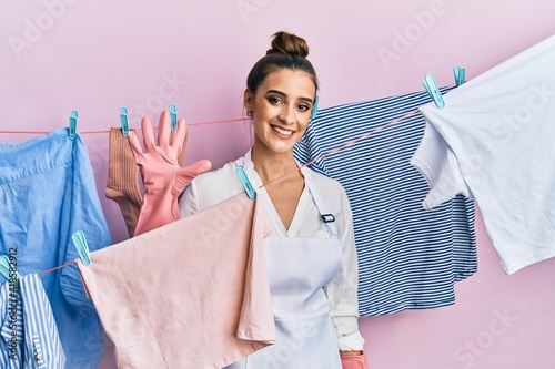 Beautiful brunette young woman washing clothes at clothesline showing and pointing up with fingers number five while smiling confident and happy.