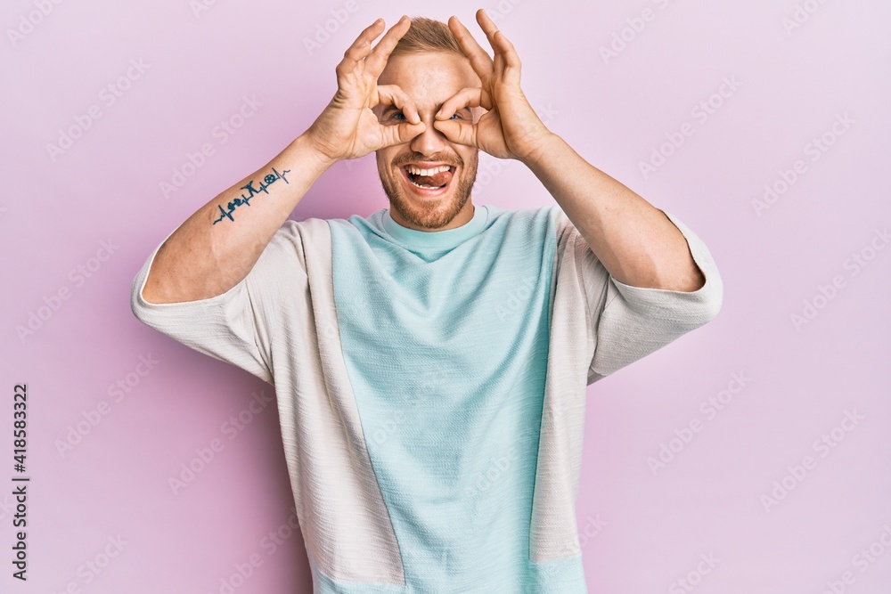 Young caucasian man wearing casual clothes doing ok gesture like binoculars sticking tongue out, eyes looking through fingers. crazy expression.