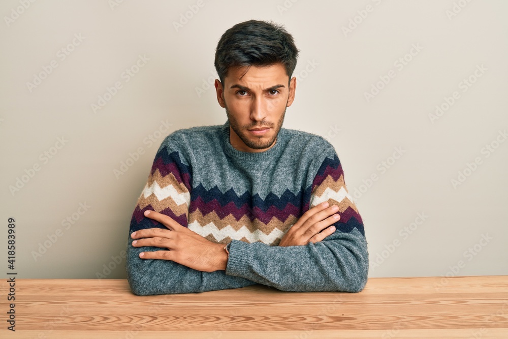 Young handsome man wearing casual sweater sitting on the table skeptic and nervous, disapproving expression on face with crossed arms. negative person.