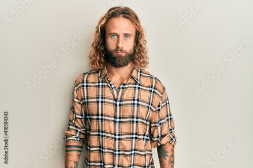 Handsome man with beard and long hair wearing casual clothes with serious expression on face. simple and natural looking at the camera.