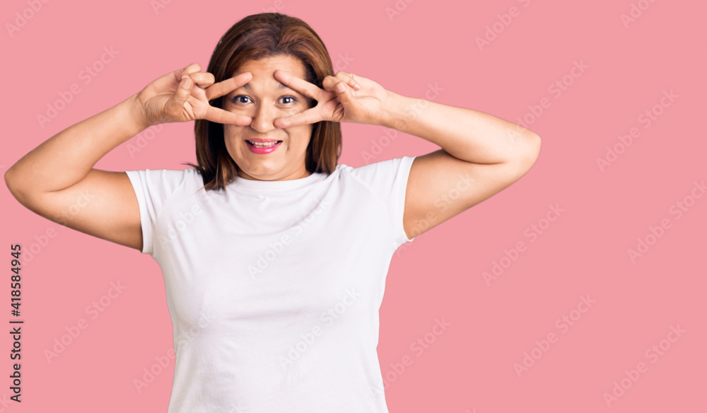 Middle age latin woman wearing casual white tshirt doing peace symbol with fingers over face, smiling cheerful showing victory Middle age latin woman wearing casual white tshirt doing peace symbol with fingers over face, smiling cheerful showing victory