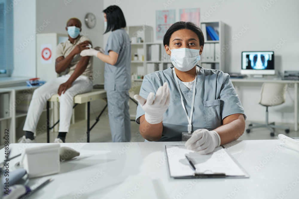 Young mixed-race clinician in protective workwear looking at you during medical consultation
