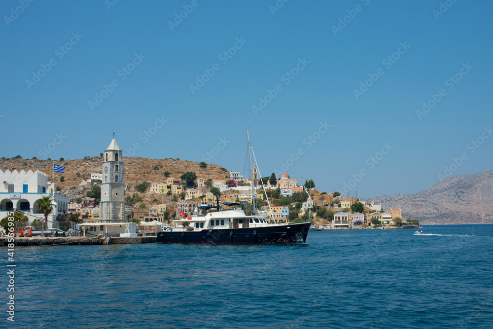View of colorful Symi island with a big black ship. Symi, Dodecanese, Greece