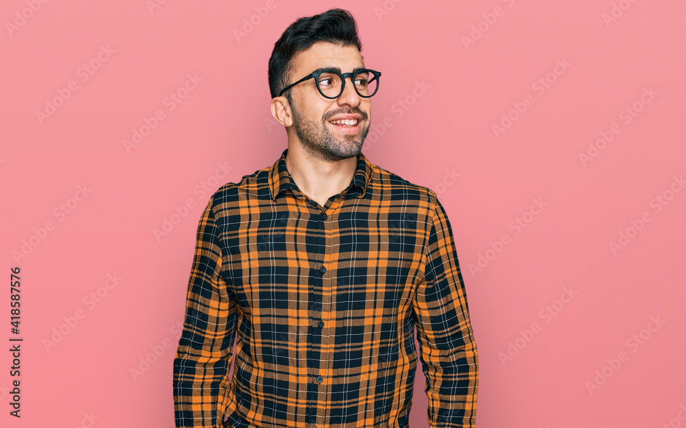 Hispanic man with beard wearing casual clothes and glasses looking away to side with smile on face, natural expression. laughing confident. Hispanic man with beard wearing casual clothes and glasses looking away to side with smile on face, natural expression. laughing confident.
