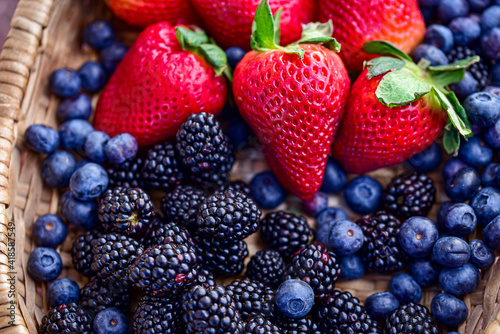 Fototapeta Naklejka Na Ścianę i Meble -  red strawberries with green leafy tops, surrounded by ripe blueberries and blackberries