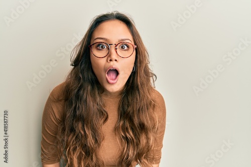 Young hispanic girl wearing casual clothes and glasses afraid and shocked with surprise and amazed expression, fear and excited face.