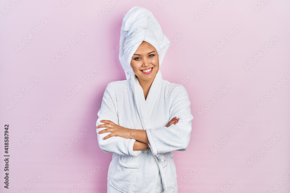 Young hispanic girl wearing shower towel cap and bathrobe happy face smiling with crossed arms looking at the camera. positive person. Young hispanic girl wearing shower towel cap and bathrobe happy face smiling with crossed arms looking at the camera. positive person.