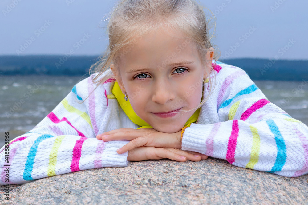 Portrait of a girl with blond long hair outside. The girl sitting on the big stone, put her head and hands on a stone. Portrait of a girl with blond long hair outside. The girl sitting on the big stone, put her head and hands on a stone.