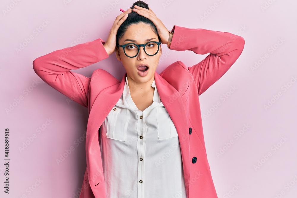 Beautiful middle eastern woman wearing business jacket and glasses crazy and scared with hands on head, afraid and surprised of shock with open mouth Beautiful middle eastern woman wearing business jacket and glasses crazy and scared with hands on head, afraid and surprised of shock with open mouth