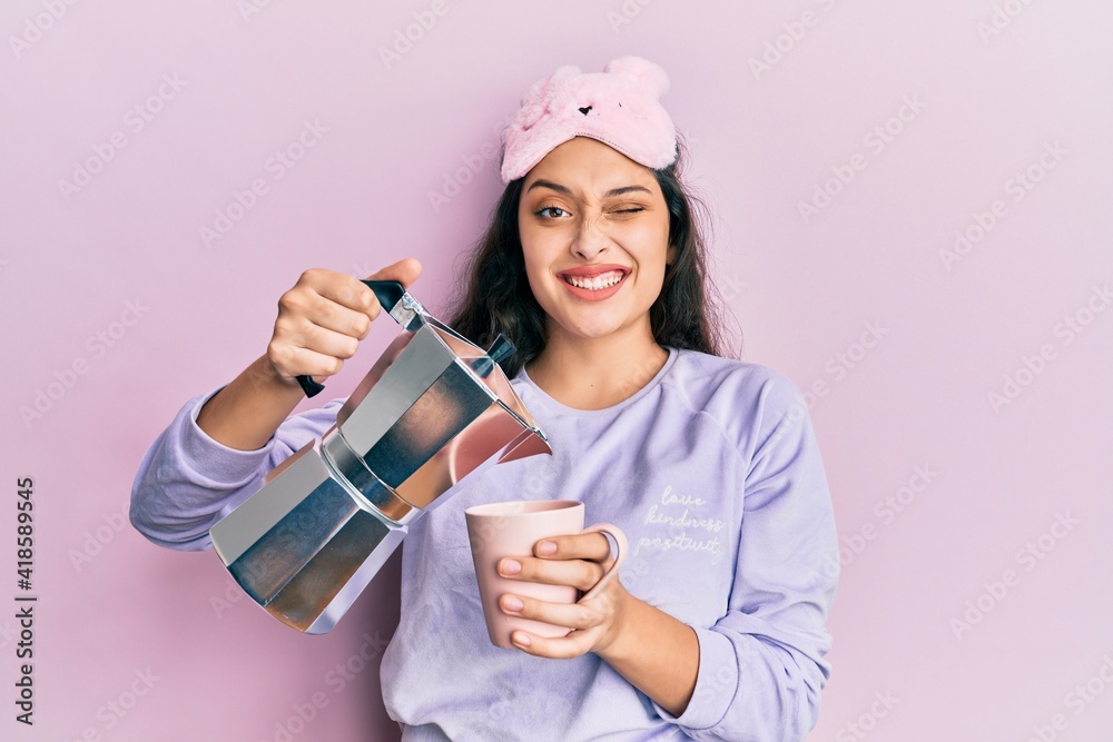 Beautiful middle eastern woman wearing sleep mask and pyjama drinking coffee winking looking at the camera with sexy expression, cheerful and happy face. Beautiful middle eastern woman wearing sleep mask and pyjama drinking coffee winking looking at the camera with sexy expression, cheerful and happy face.