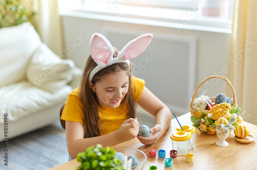 Cute little child wearing bunny ears painting eggs.