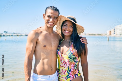 Young latin couple wearing swimwear  smiling happy and hugging at the beach.