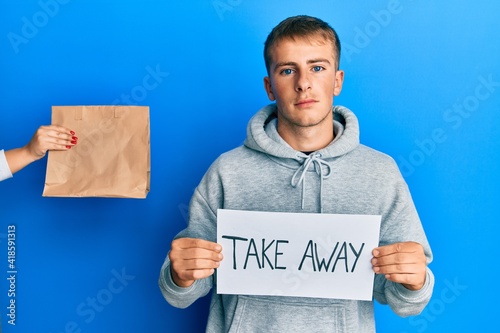 Young caucasian man holding take away banner reciving delivery paper bag relaxed with serious expression on face. simple and natural looking at the camera. photo